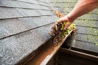 Blocked gutters and a roofer is trying to unblock them by removing waste material
