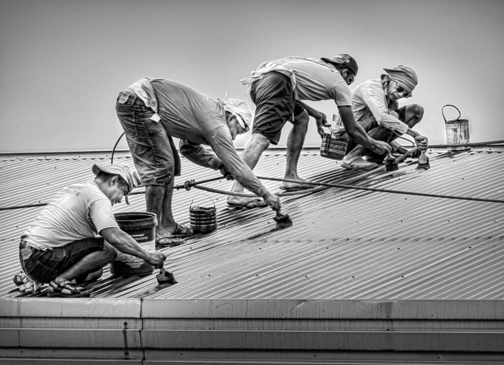 Four Filipino men paint a corregated metal room of an eight-story building in Malate, Philippines, wearing sandals and with only one rope for safety.