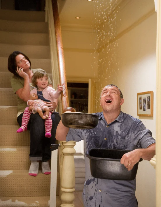 man holding buckets to control leaking roof, woman holding baby and calling roof repair company