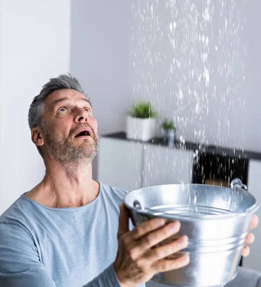 man holding bucket to control roof leak while looking up