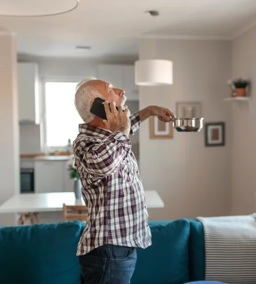 Old man holding pan under leaking roof while making a call