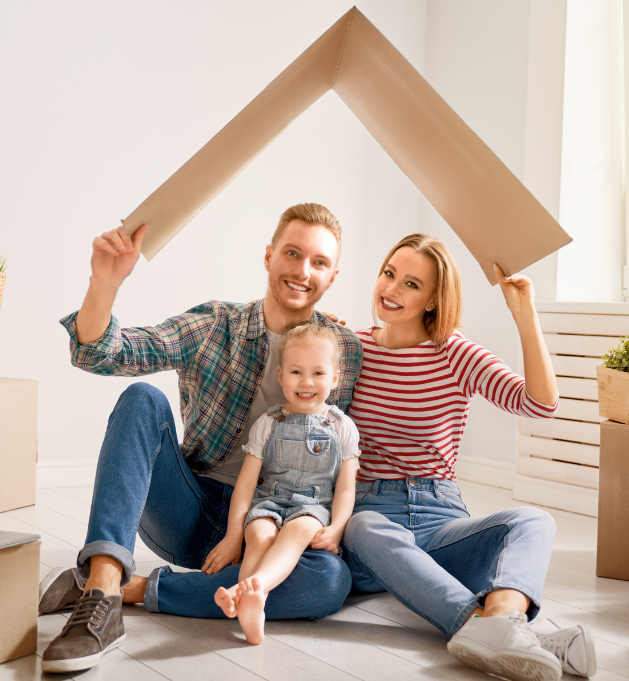 A family of three, with the father and mother holding a cardboard roof over their baby.