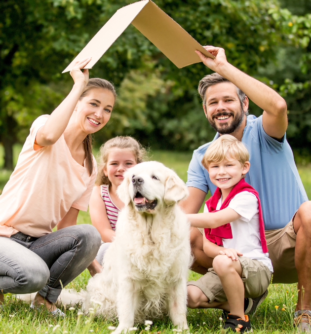 Man and wife holding cardboard roof over their two kids and dog while squating.