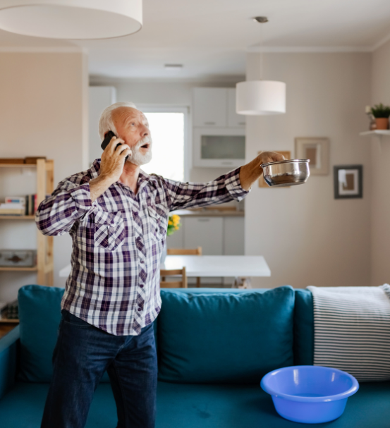 man holding buckets to control leaking roof while phoning for help