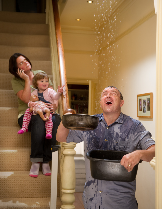 man holding buckets to control leaking roof, woman holding baby and calling roof repair company