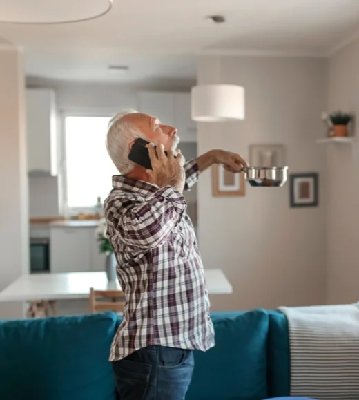 Old man holding pan under leaking roof while making a call